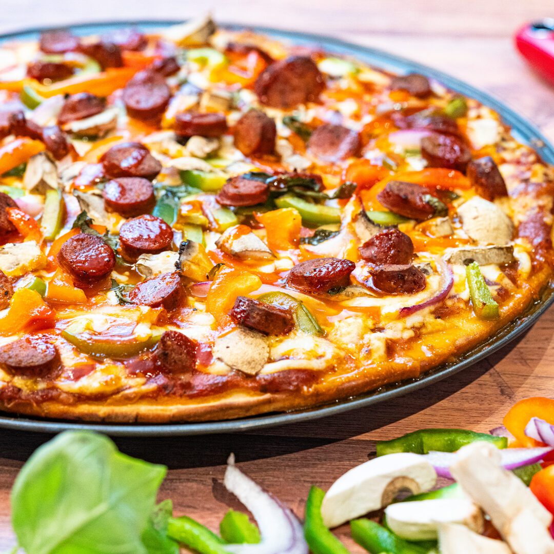 La photo représente la recette : Pizza maison à la sauce BBQ, champignons de Paris et merguez